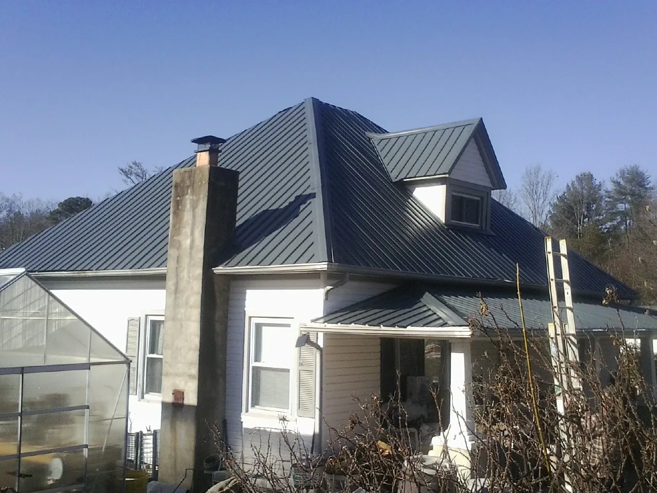 Dark blue standing seam metal roof on a white farmhouse with dormer — Slate & Tile Roof Repair by Roofing Brothers in Compton