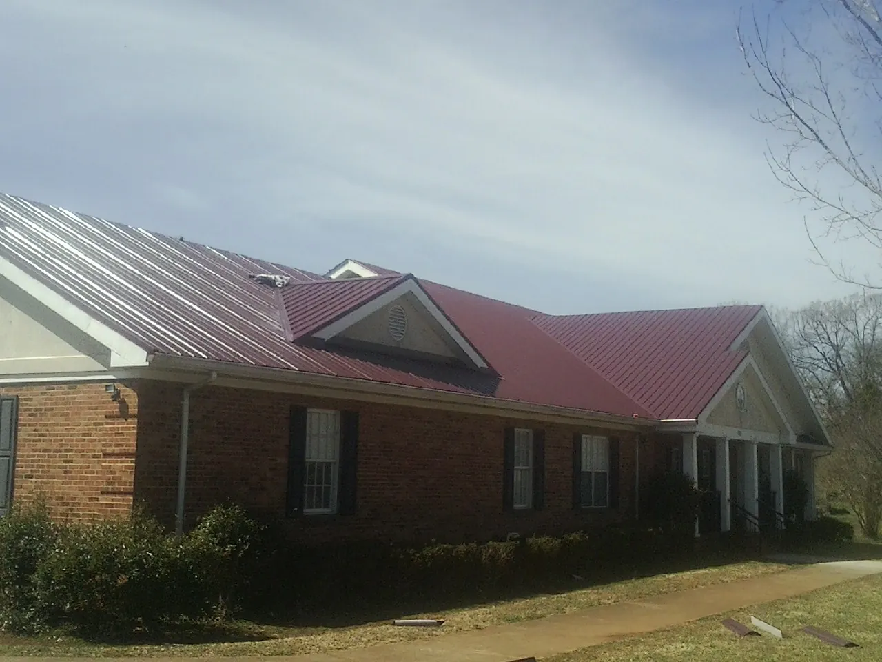Red metal roof with gabled entries on a long brick building, from a Hail Damage Roof Repair job in Compton