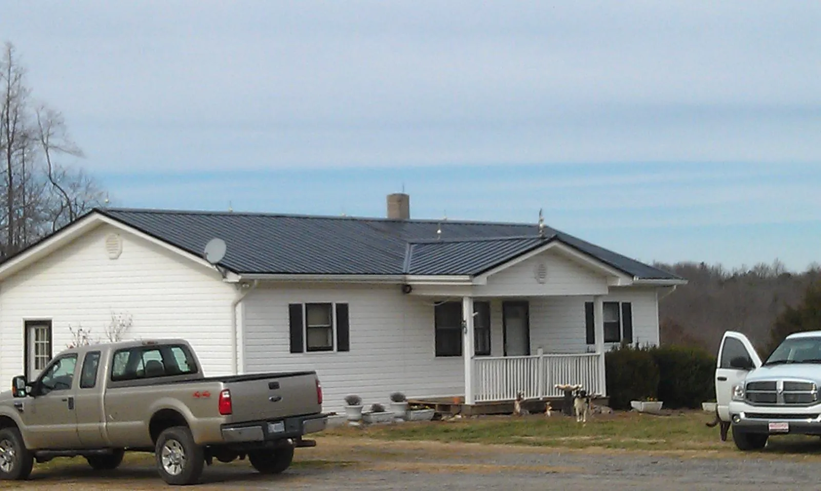 Finished dark metal roof on a white ranch home with work trucks parked in Compton