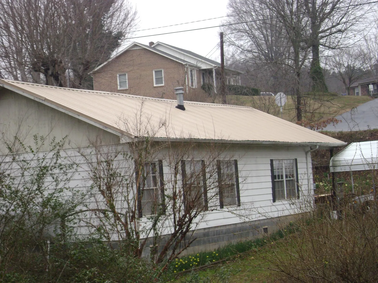 Tan metal roof on a white sided house set into a hillside — Commercial Roofing by Roofing Brothers in Compton